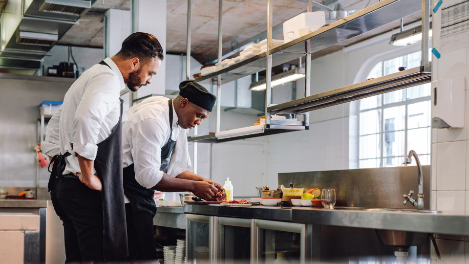 Un chef latino y su asistente preparando un plato.